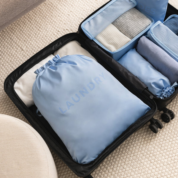 light blue laundry bag displayed in a suitcase on a beige carpet. 