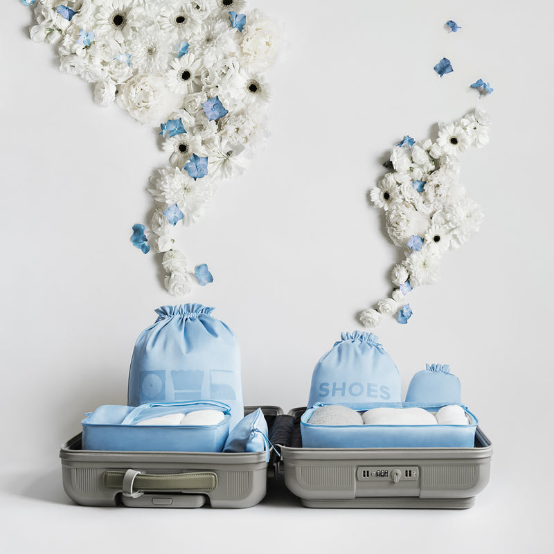 Light blue packing bags in a suitcase in front of white and blue flowers. 