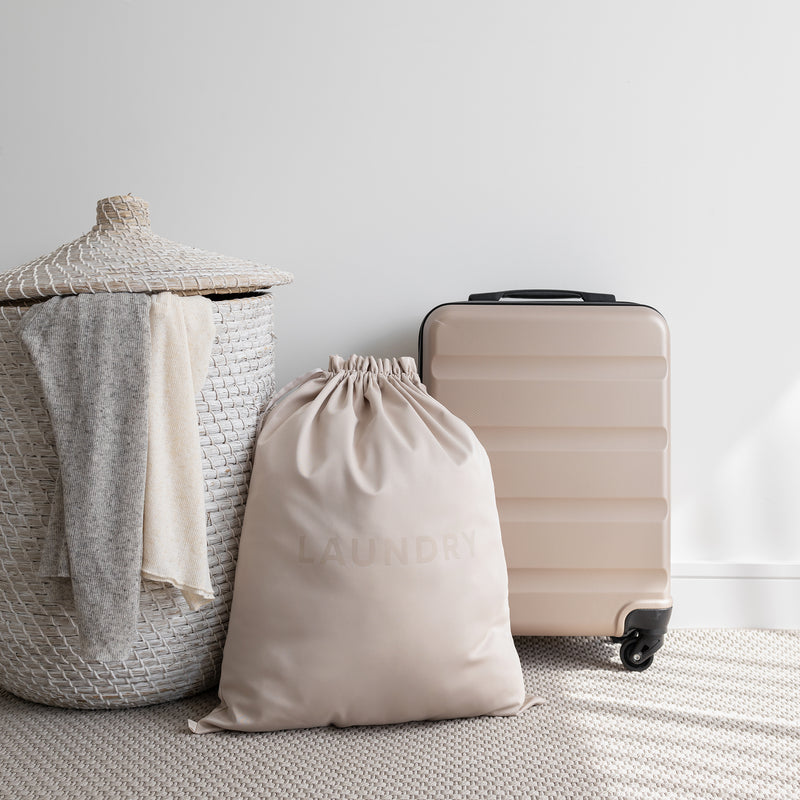 Extra large laundry bag in the color beige beside a basket and a suitcase