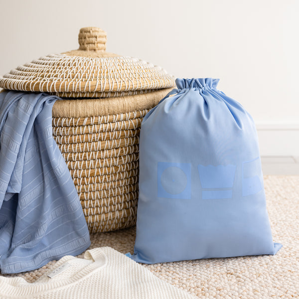 Large blue laundry bag in front of a beige laundry basket.